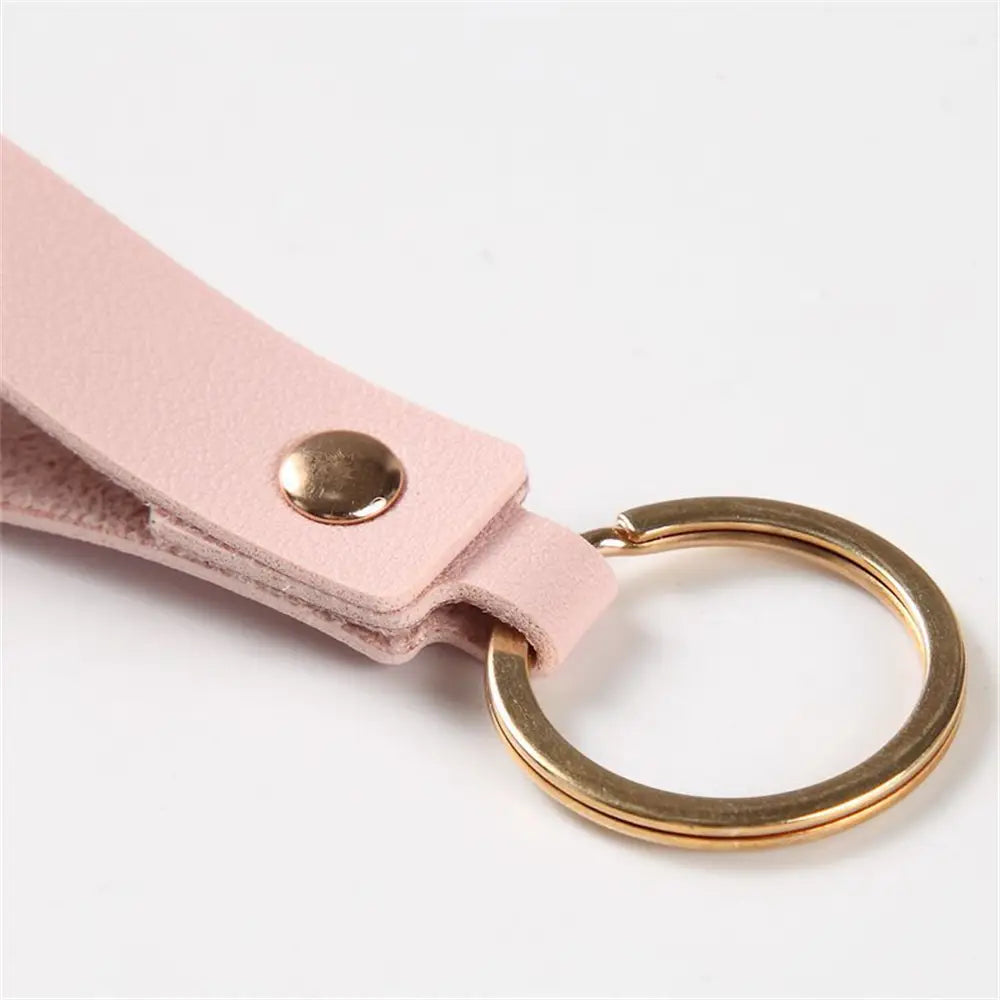 A delicate pink pu leather keychain featuring a gold-toned metal ring and snap button for fashionable key organization.