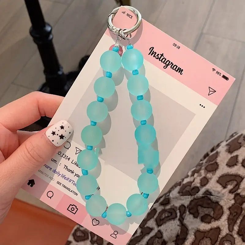 Eine zarte türkisfarbene, frostglasartige Glasperlen-Handy-Handgelenksschlaufe mit kleinen blauen Akzentperlen und einem silbernen Metallring als Charm.