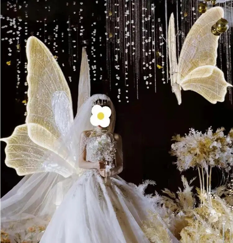 Ein schimmerndes weißes Hochzeitskleid mit kunstvoll gearbeiteter Peretten-Spitzen-Bodice und fließendem Tüllrock, dargestellt unter leuchtenden Schmetterlingsflügeln, hängende Hochzeitstennenlichtanlage.