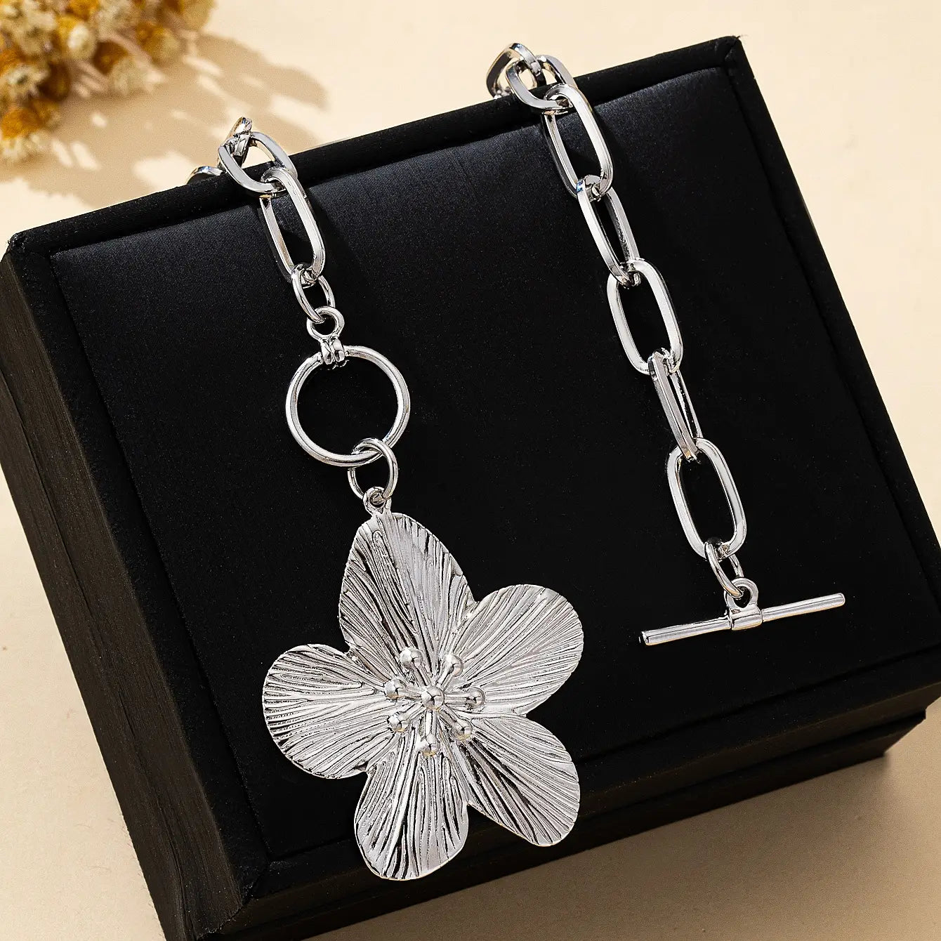 Collier pendentif à chaîne argentée présentant un pendentif de fleur de glycine à cinq pétales, style vintage, avec des feuilles texturées et une fermeture à t-bar pour femmes.