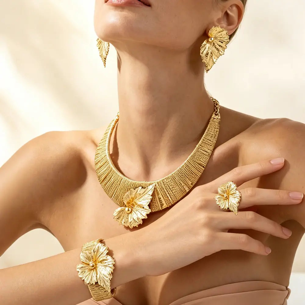 Parure de bijoux en perles et feuilles d’or, comprenant un collier statement inspiré des feuilles métalliques dorées, des boucles d’oreilles assorties et un bracelet, avec des détails complexes.