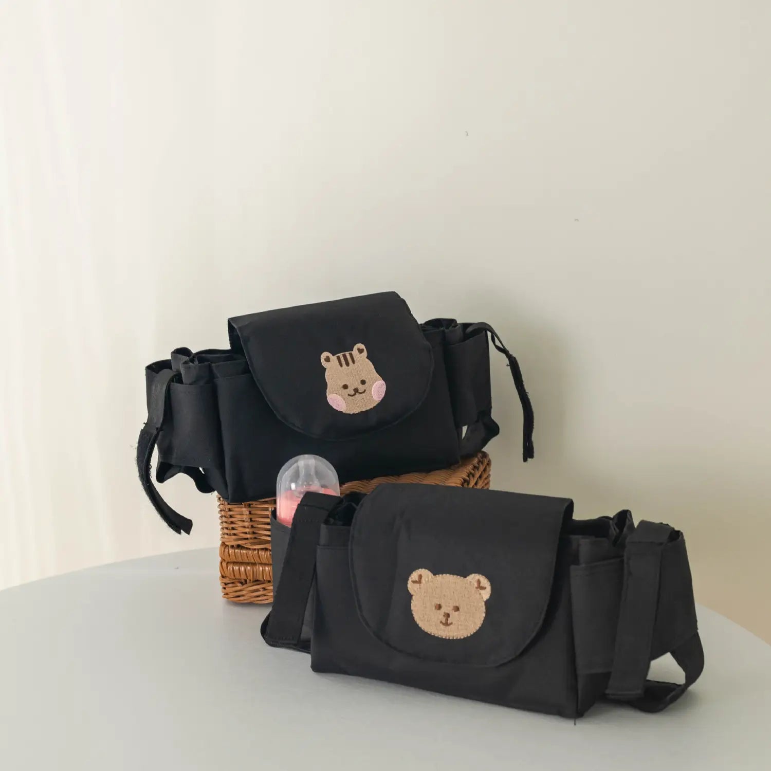 ベビーの着替えに必要な小物を収納するための、刺繍入りのクマの顔デザインが施されたブラックの布製ベビーカー用オーガナイザーバッグ。