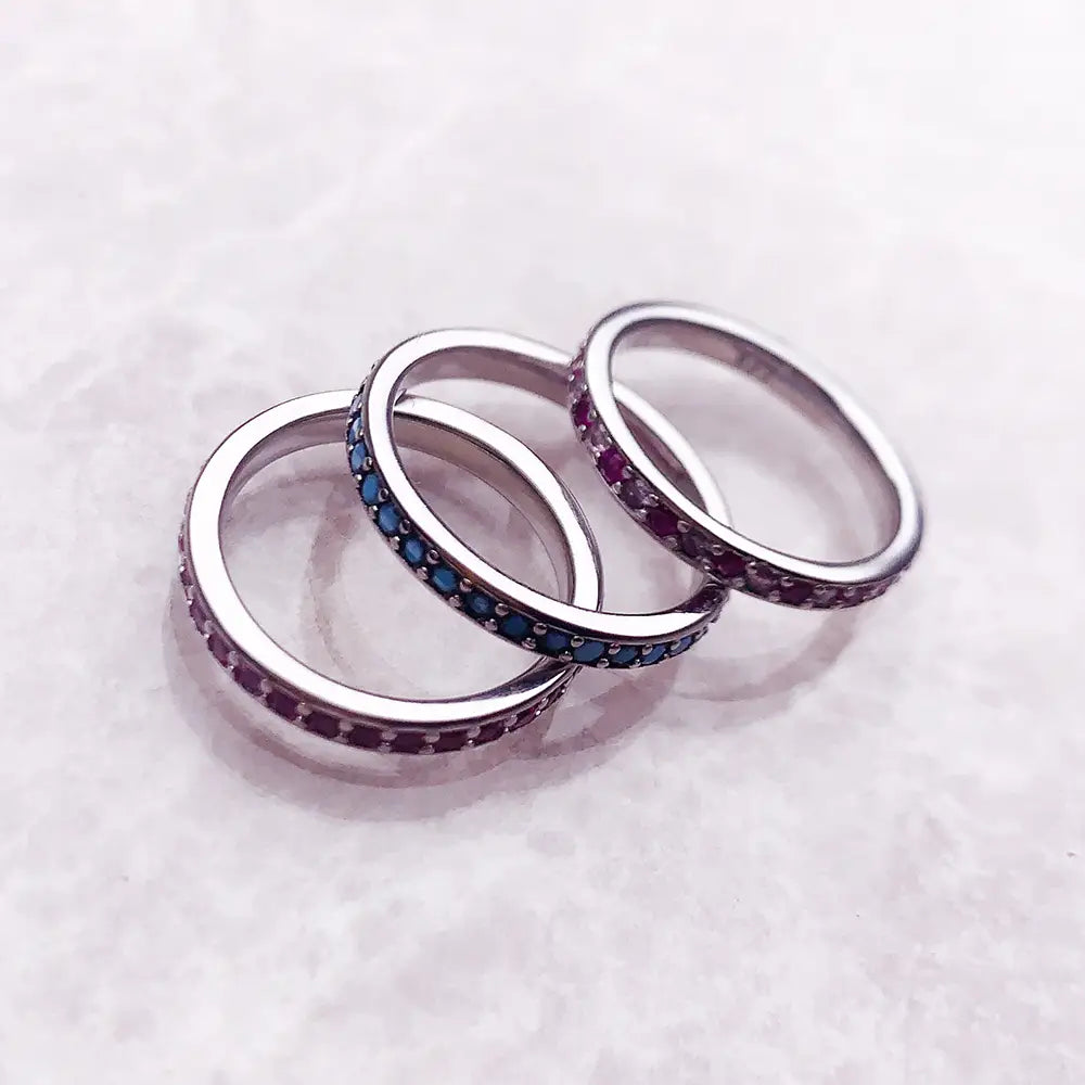 Bague empilée en argent sterling sertie d’une pierre précieuse, comportant trois anneaux en argent empilés, ornés de rangées continues de petites pierres précieuses bleues et violettes.