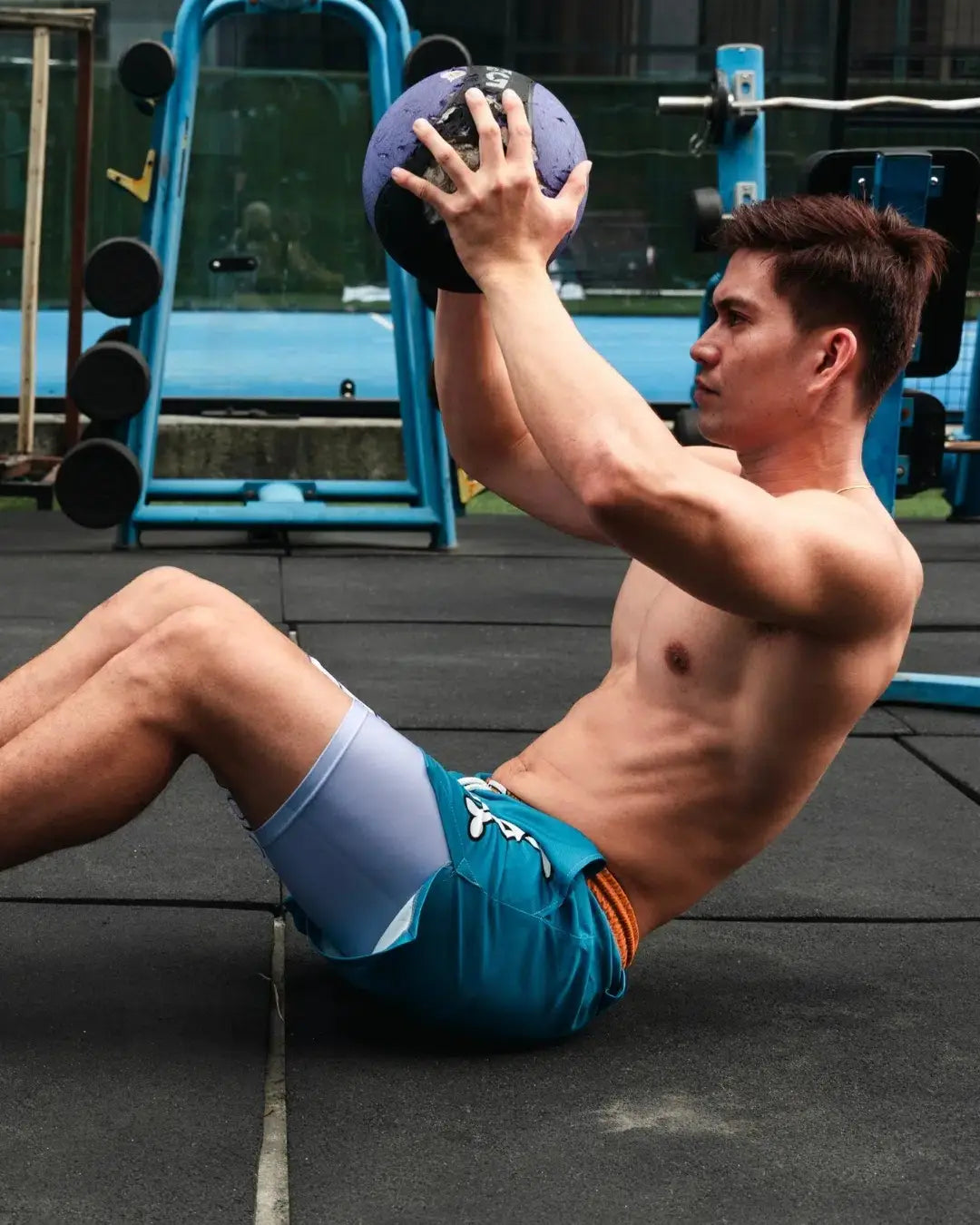 balón medicinal lastrado morado y negro que se muestra con pantalones cortos de gimnasia Digimon Bandai Weregarurumon, destacando equipo para acondicionamiento físico y entrenamiento de fuerza.