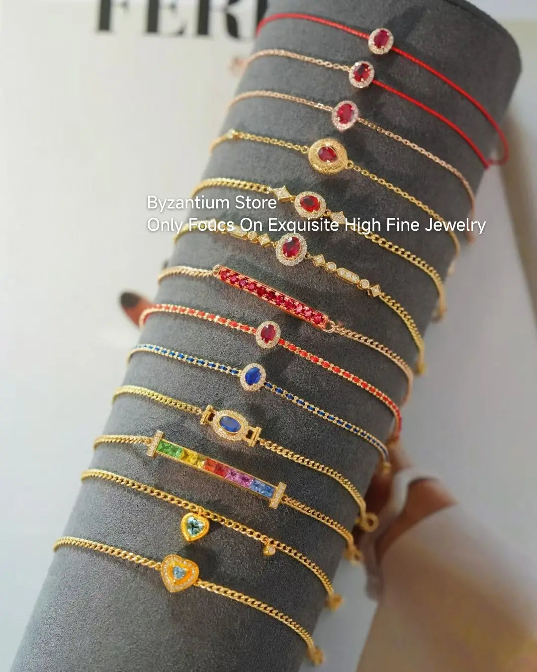 Eine Sammlung goldfarbener, zarter Armbänder mit farbigen Edelsteinakzenten und aufwendigen Designs, präsentiert auf einem grauen Samtständer neben Ohrringen mit silbernen Tropfenquasten in Gold-Vermeil.