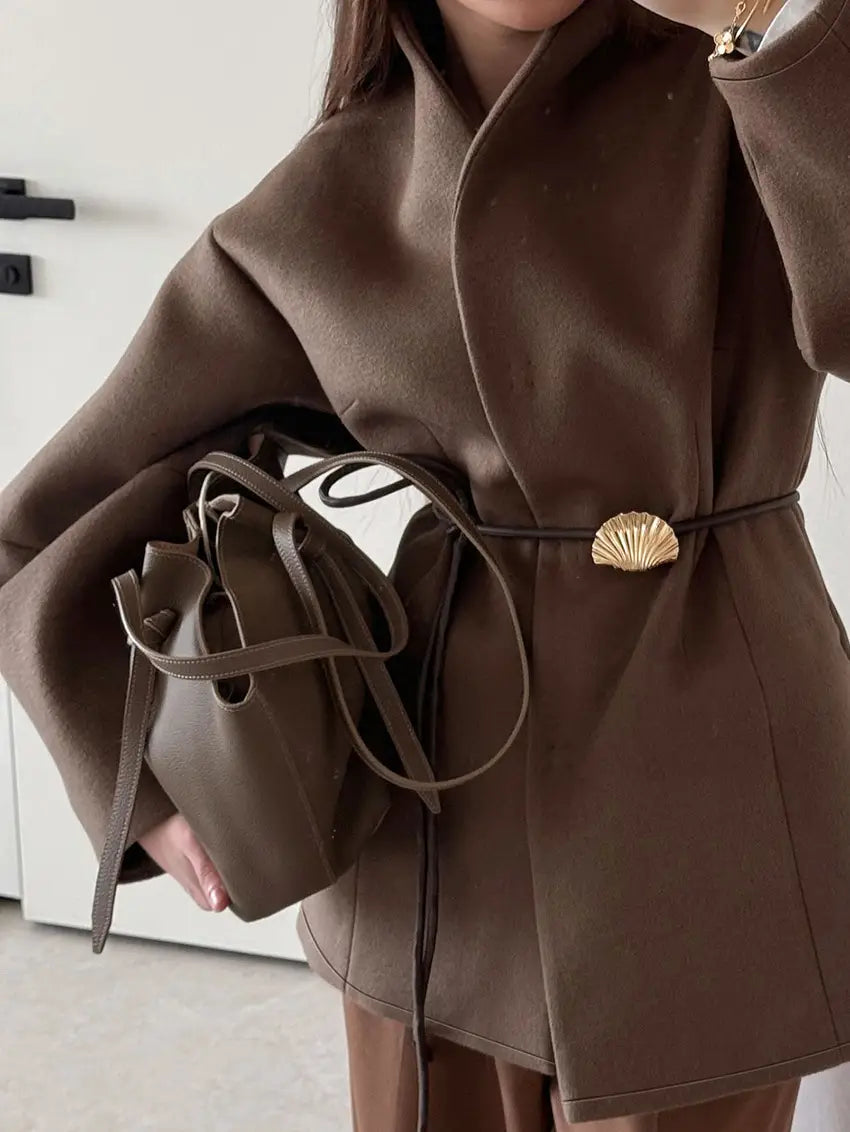 Brown leather bucket bag with drawstring closure and matching belt strap featuring gold-toned shell-shaped buckle paired with wool belted coat brown winter jacket.