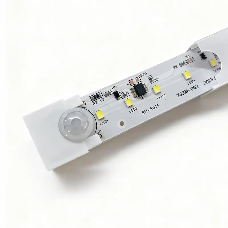 Lámpara lineal LED de plástico blanco con sensor de movimiento integrado y componentes visibles de placa de circuito, mostrada desde el frente