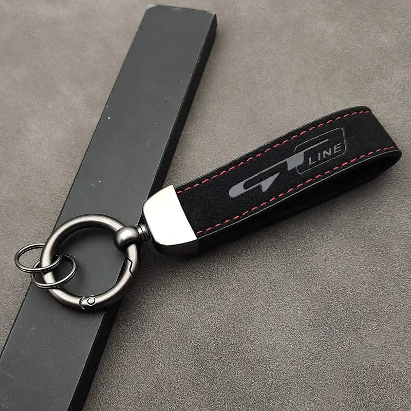 Schwarzer Wildleder-Schlüsselanhänger der GT Line mit roter Steppnaht, silbernem Logo, Metallring und Karabinerhaken.