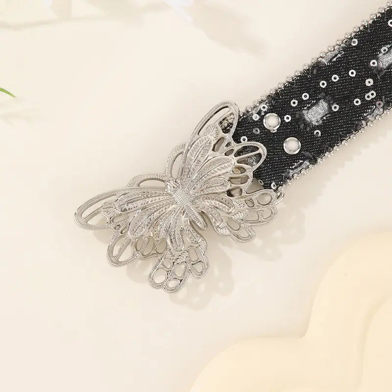 Boucle de ceinture en forme de papillon argentée, avec un motif de filigrane complexe, fixée à une taille élastique noire à sequins, rehaussée de strass argentés — ceinture en cuir papillon y2k