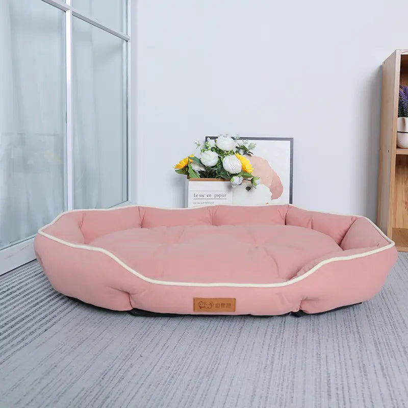 Large pink plush sofa sleeping bed for dogs with a rectangular shape, cream-colored piping, and a brown leather-like label.