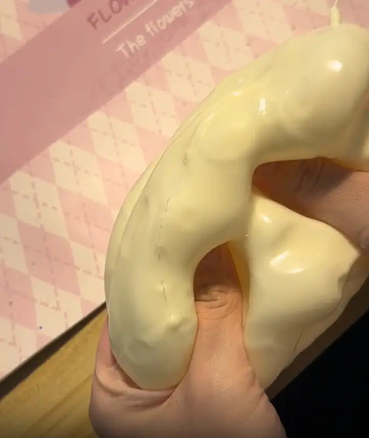 Un jouet à mâcher et à malaxer en forme de fromage, à surface brillante, blanc cassé et crème, conçu pour soulager le stress, texture molle, maintenu dans une main pour apaiser le stress lié au jouet.