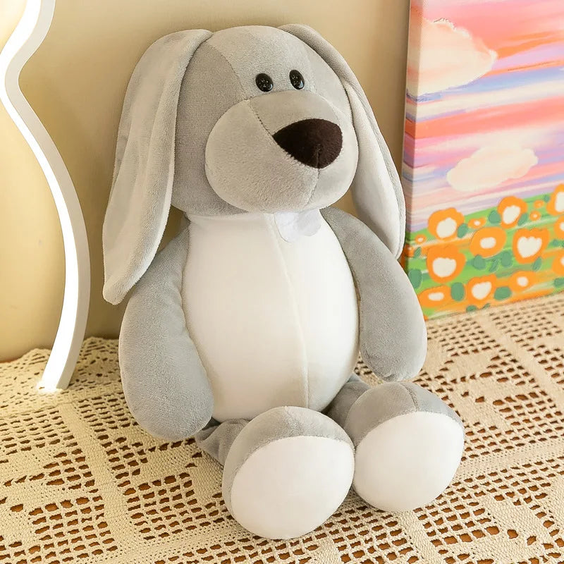 Un suave peluche de animal de la jungla gris claro con forma de conejo, con ojos negros tipo botón, vientre blanco y nariz marrón, se encuentra sobre un mantel de encaje.