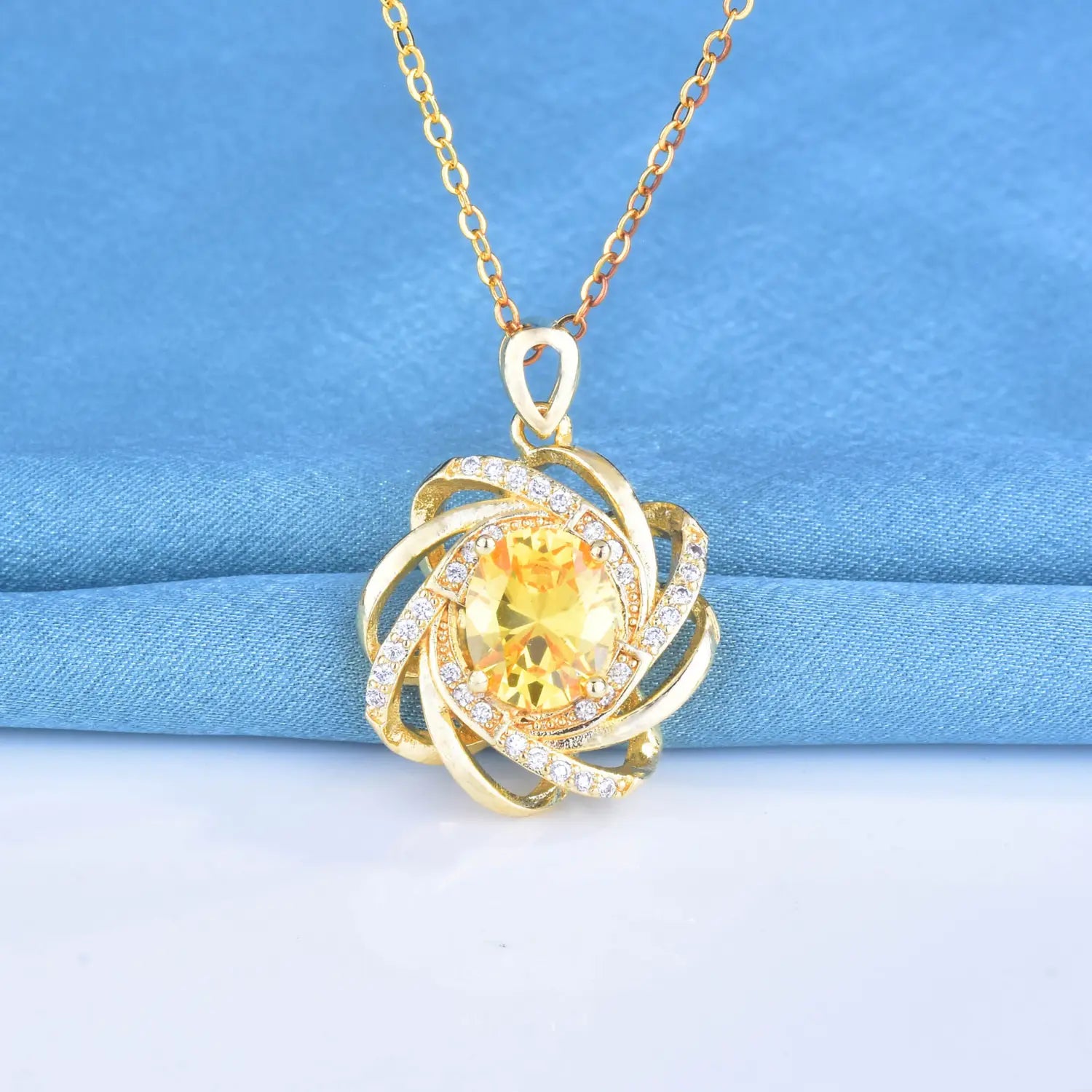 Collier pendentif moulin à vent en citrine en or, collection de pierres de naissance dorées, présentant une pierre jaune centrale entourée de bandes métalliques dorées tourbillonnantes et de petites pierres transparentes.
