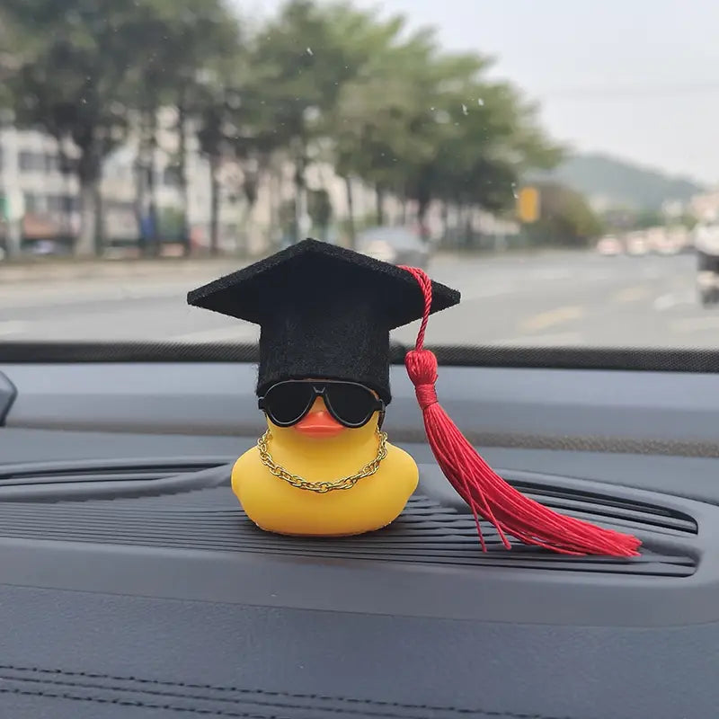 Yellow rubber graduation rubber duck car dashboard ornament wearing a black graduation cap with red tassel sunglasses and a gold chain.