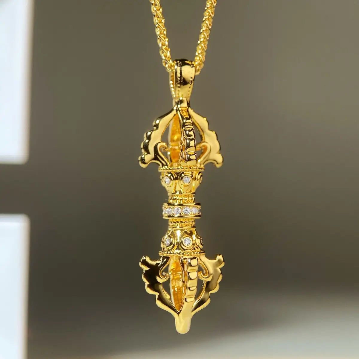 24kゴールドの金剛杵ダイヤモンド・ペンダントネックレスのデザイン。精巧な細工が施されたゴールドのチベット祈祷輪ペンダントネックレスで、同色のゴールドチェーンに吊り下げられ、はっきりとした宝石が配されています。