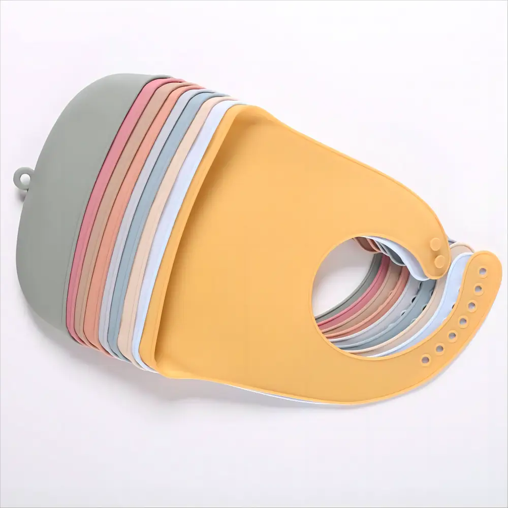 Ein Stapel wasserfester, verstellbarer Silikon-Lätzchen für Babys in Pastellgelb, Rosa, Blau und Grau, einschließlich einer beigen Option.