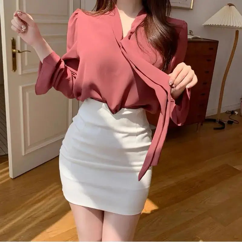Eine zartrosa satinierte Bluse mit V-Ausschnitt und fließenden Ärmeln, kombiniert mit einem Mini-Bleistiftrock mit hoher Taille