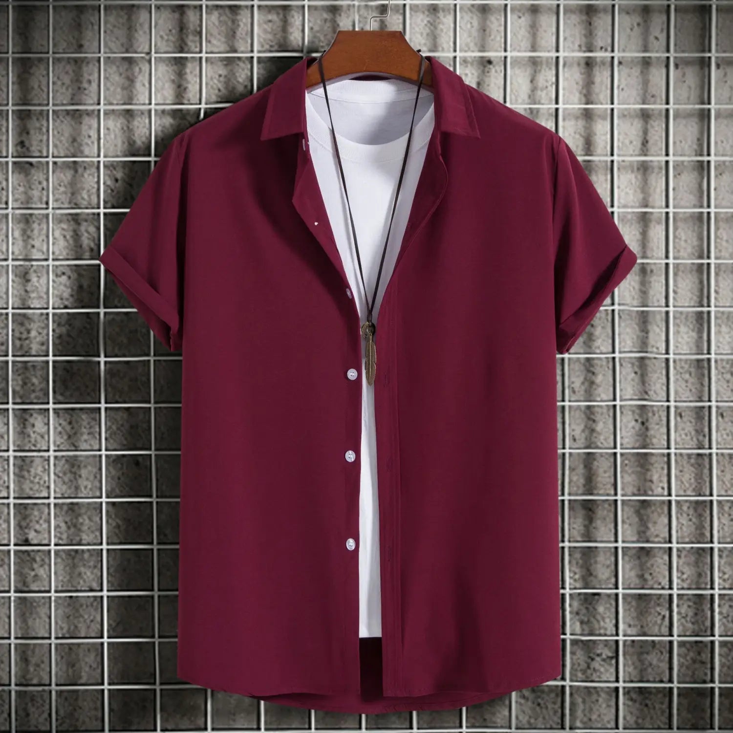 Chemise bordeaux à manches courtes pour homme, style mode, unie, avec boutons et col, portée sur un t-shirt blanc, affichée sur un cintre en bois, idéale comme chemise de plage décontractée.