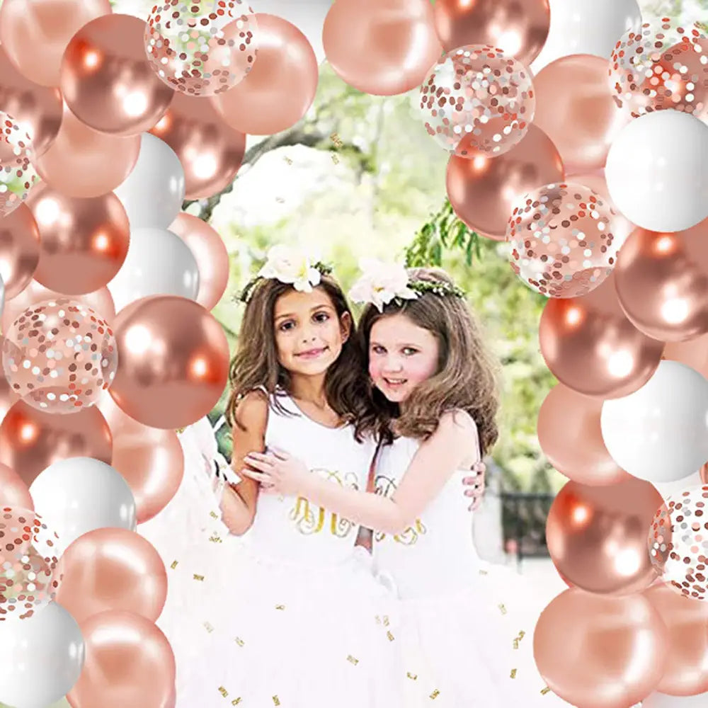 Roségold- und weiße mit Konfetti gefüllte Ballons bilden in einer Partyddeko aus dem Roségold-Konfetti-Ballonset einen festlichen Torbogen.