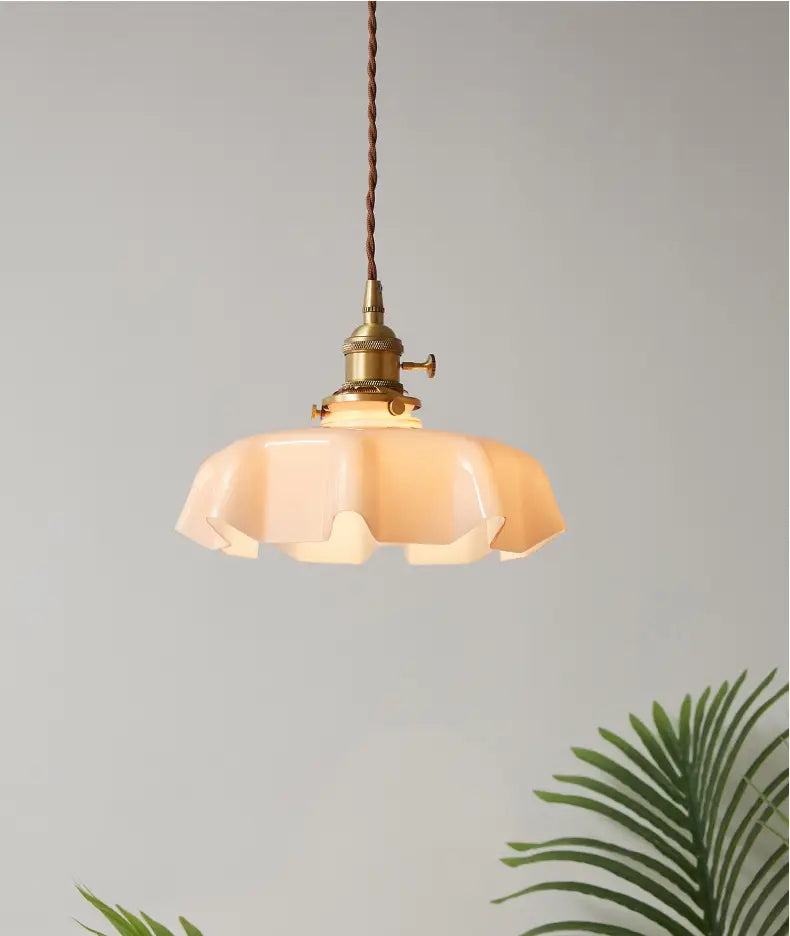 Un luminaire suspendu à jupe florale en verre à tonalité chaude avec une conception en forme de pétales, une tête de lampe en cuivre à finition laiton et un cordon brun torsadé, vu depuis un angle avant.