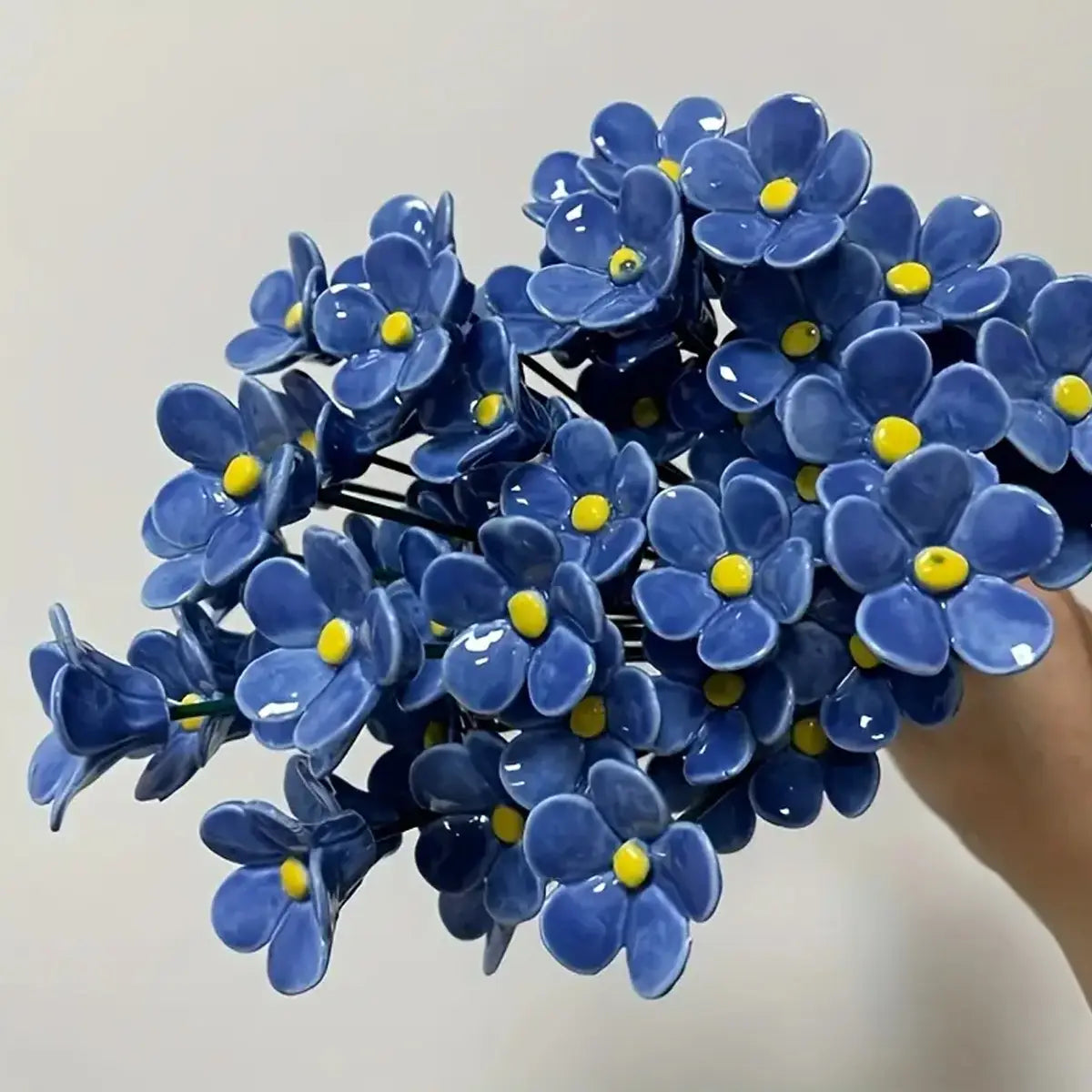 a glossy blue ceramic bouquet of artificial flowers featuring forget me nots with bright yellow centers ideal for decorating vases