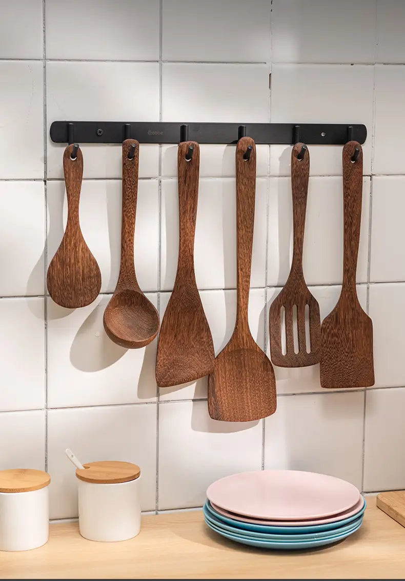 Set of six dark brown wooden kitchen utensils hanging on a black metal rack designed for use with non-stick cookware.