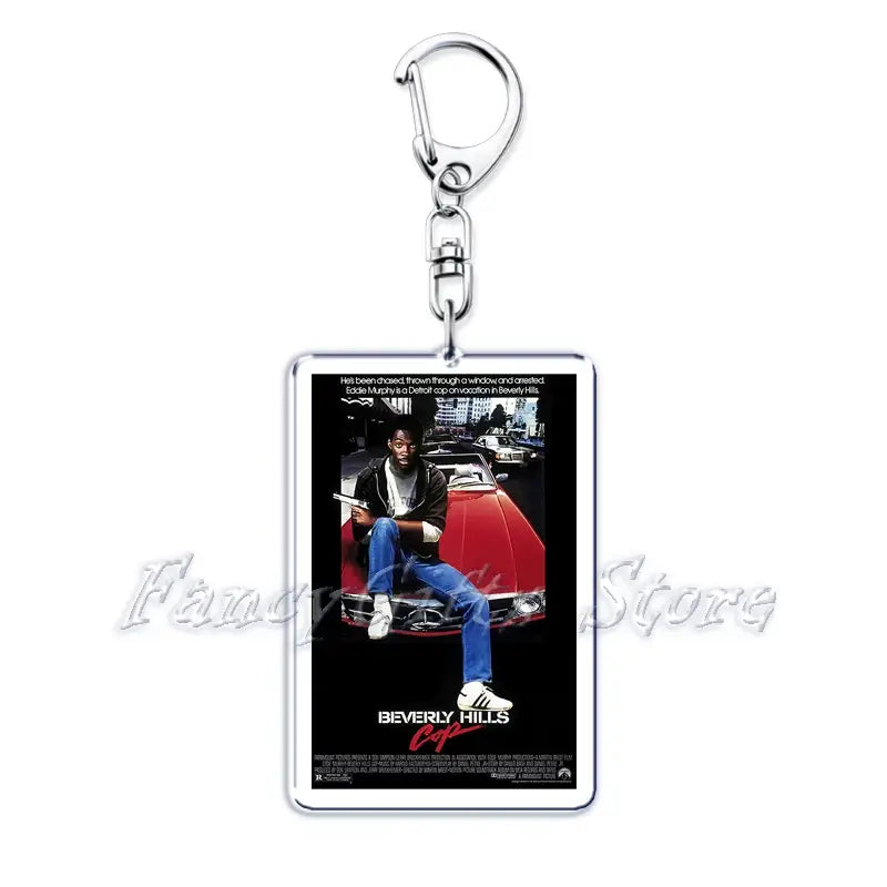 rectangular acrylic keychain featuring the beverly hills cop movie poster with eddie murphy in a black jacket and blue jeans sitting on a red car from the movie poster acrylic keychain set.