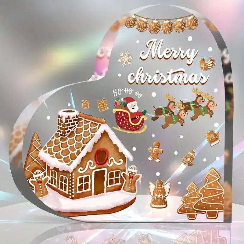 Soporte para adorno de escritorio en forma de corazón navideño de acrílico, que presenta un adhesivo transparente para ventana con forma de corazón, con una casa de pan de jengibre, Santa en su trineo con renos, copos de nieve y texto de “Feliz Navidad”.