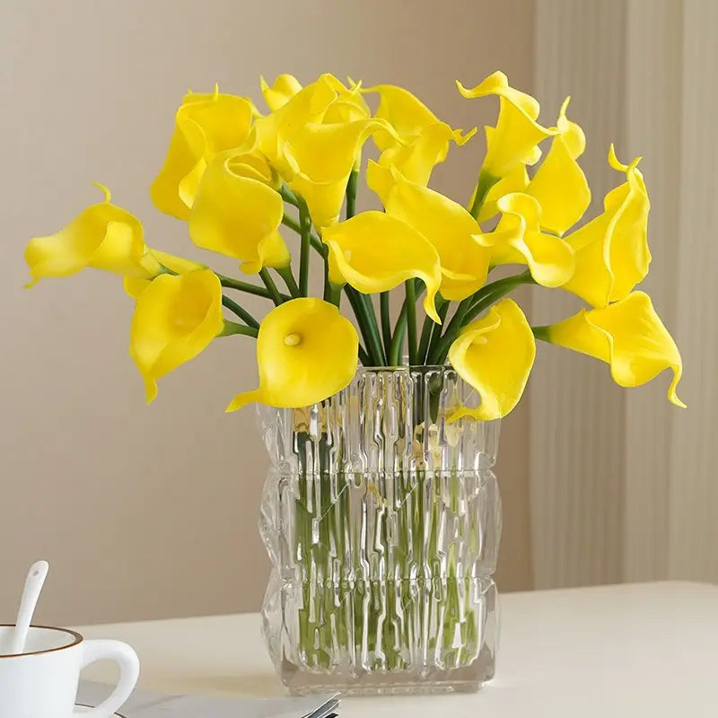a clear textured glass vase filled with vibrant yellow calla lily flower bouquet for home decor viewed from the front