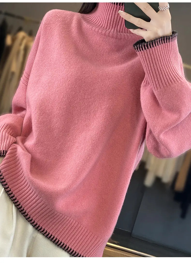 A soft pink pure wool turtleneck sweater for women features a loose fit with ribbed cuffs and hem accented by a subtle black striped trim.