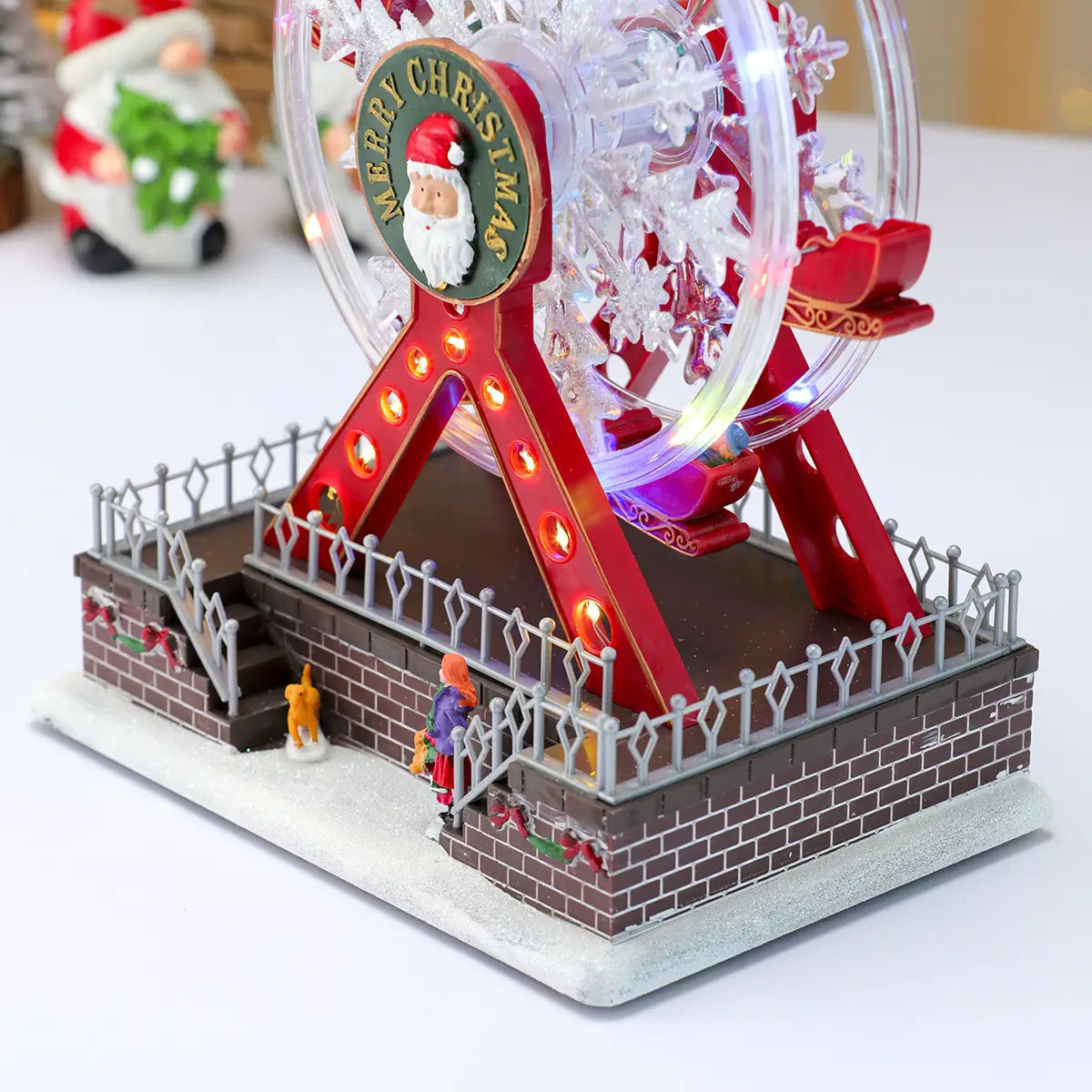 Ornement de manège forain musical de Noël présentant des lumières LED rouges et transparentes, avec un emblème de père Noël sur le moyeu central.