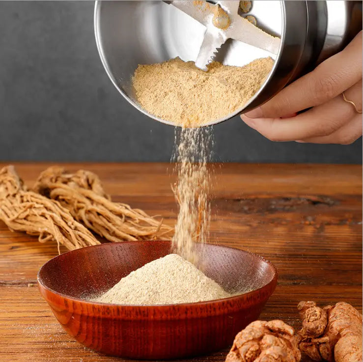 a stainless steel electric coffee and spice grinder blade mill pouring light brown ground turmeric into a wooden bowl
