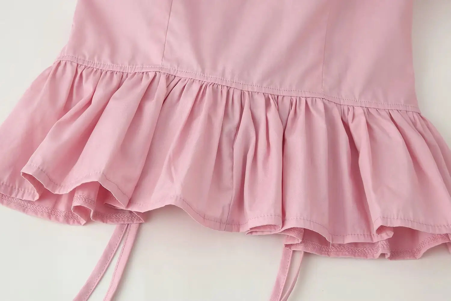 A soft pink ruffled skirt with delicate lace trim and thin matching side ties paired with a women slim-fit design long sleeve top featuring a round neckline.