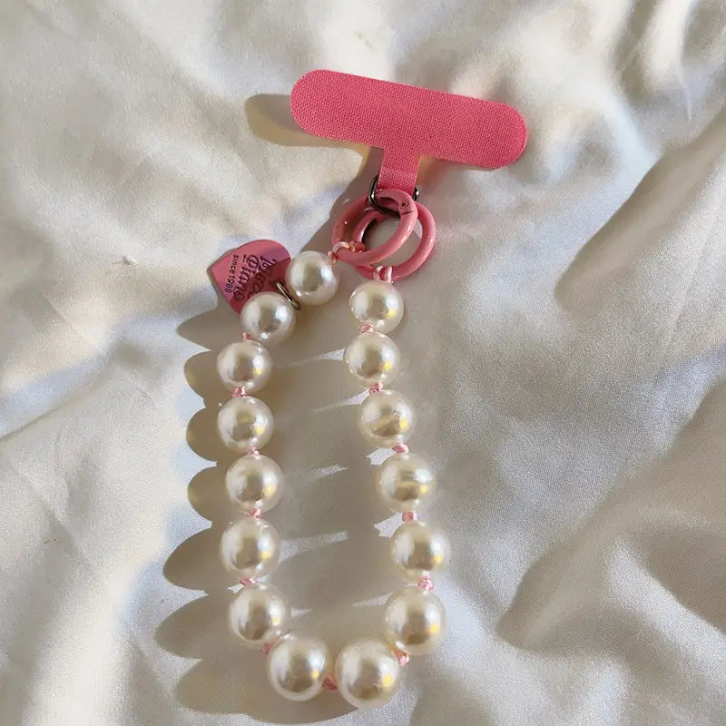 Correa de muñeca para teléfono con cuentas engarzadas color rosa con un clip a juego con forma de t y un dije con forma de corazón mostrado desde un ángulo frontal