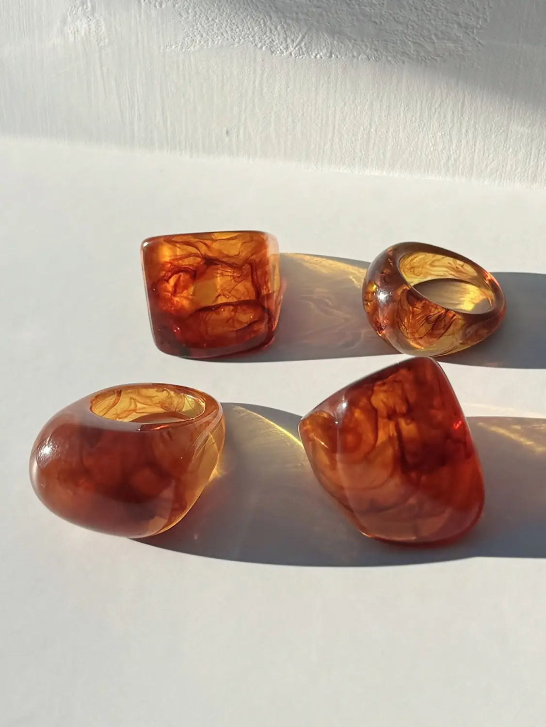 Amber-colored chunky resin cocktail rings with a marbled translucent finish and organic irregular shapes in a 4-piece set.