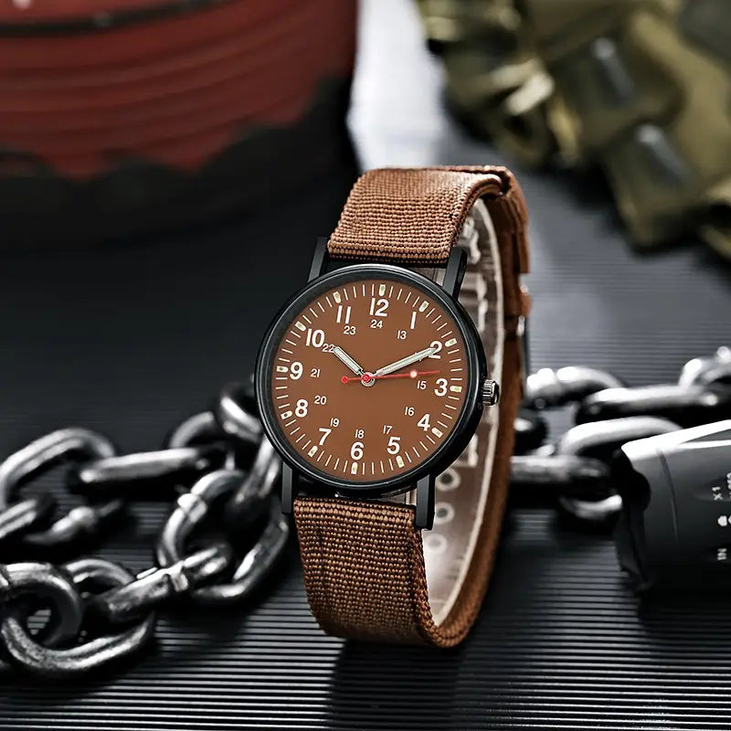 Militärisches Quarzarmbanduhr mit braunem Canvas-Armband, schwarzem Gehäuse und braunem Zifferblatt mit weißen Ziffern, dargestellt vor einem olivgrünen Nylonarmband-Untergrund.