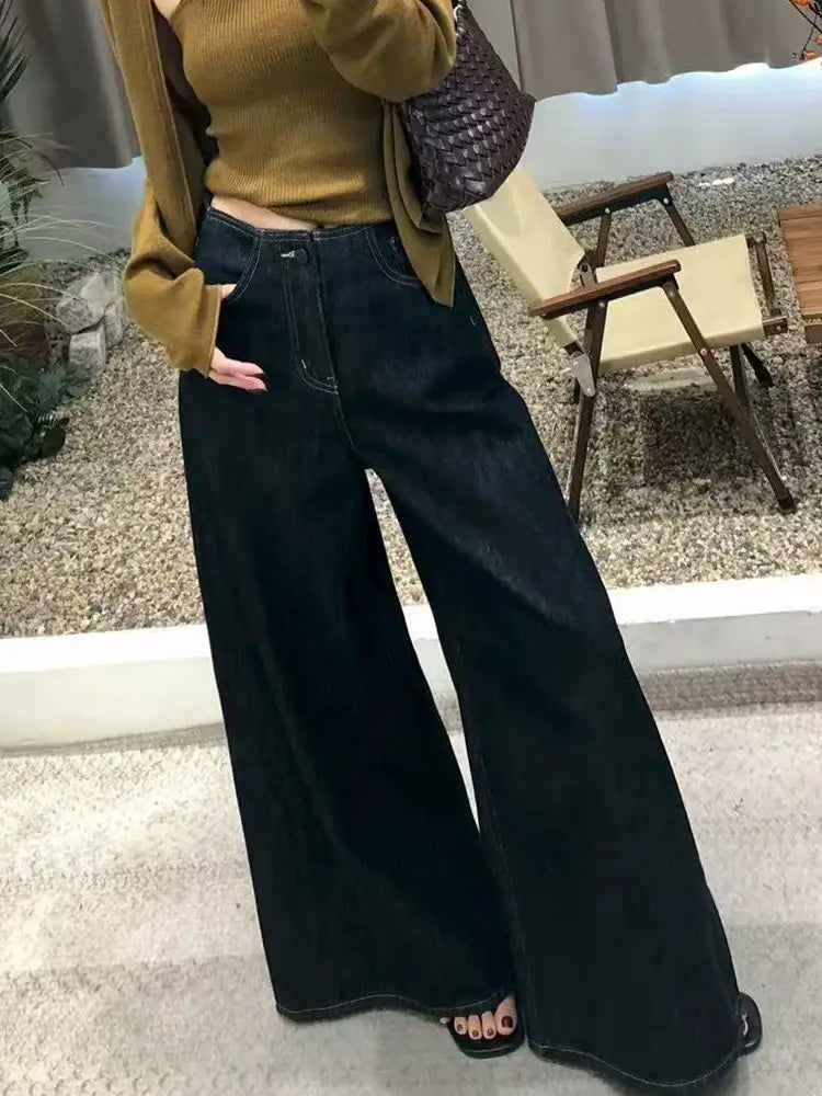 Pantalones vaqueros de tiro alto y pierna ancha de lavado oscuro para mujer, con costuras visibles en la tela vaquera.