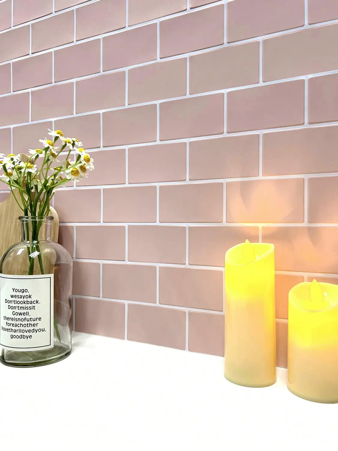 a clear glass bottle with white daisies is displayed alongside glossy white subway peel and stick tile designed for direct contact on fresh paint surfaces