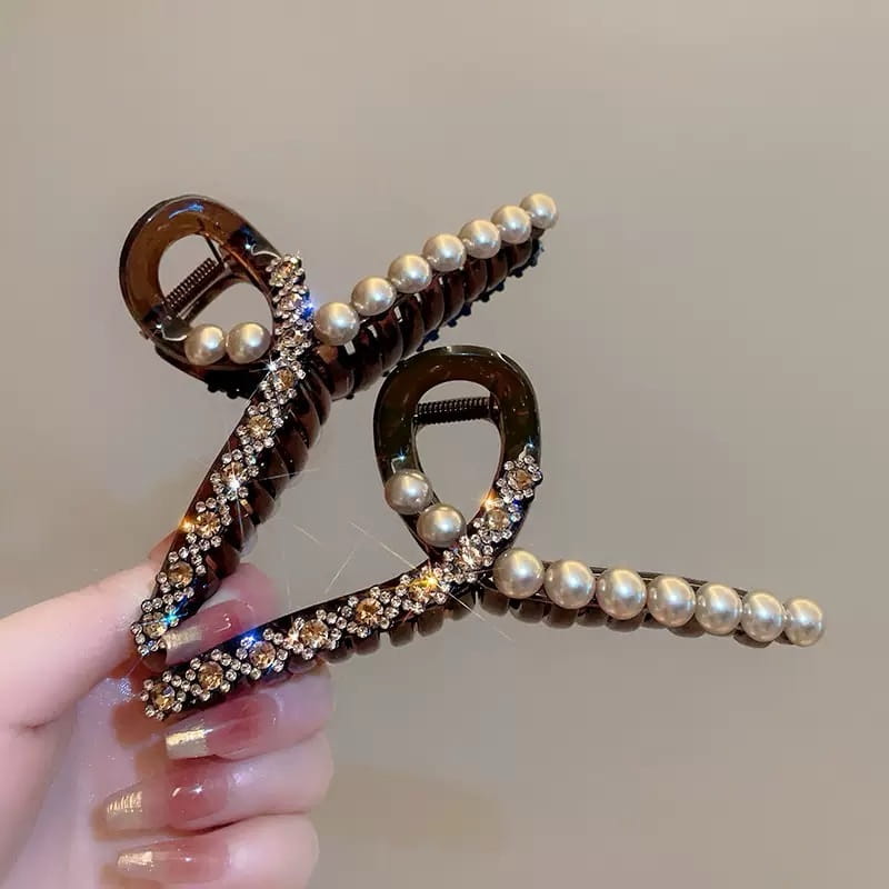 Barrette serre-cheveux glamour en écaille de tortue, ornée d’une rangée de perles blanches lustrées et de strass étincelants le long de ses bords incurvés.