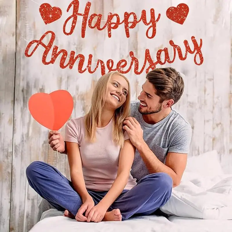 red glittery anniversary banner party decoration with heart accents displayed above a smiling couple.