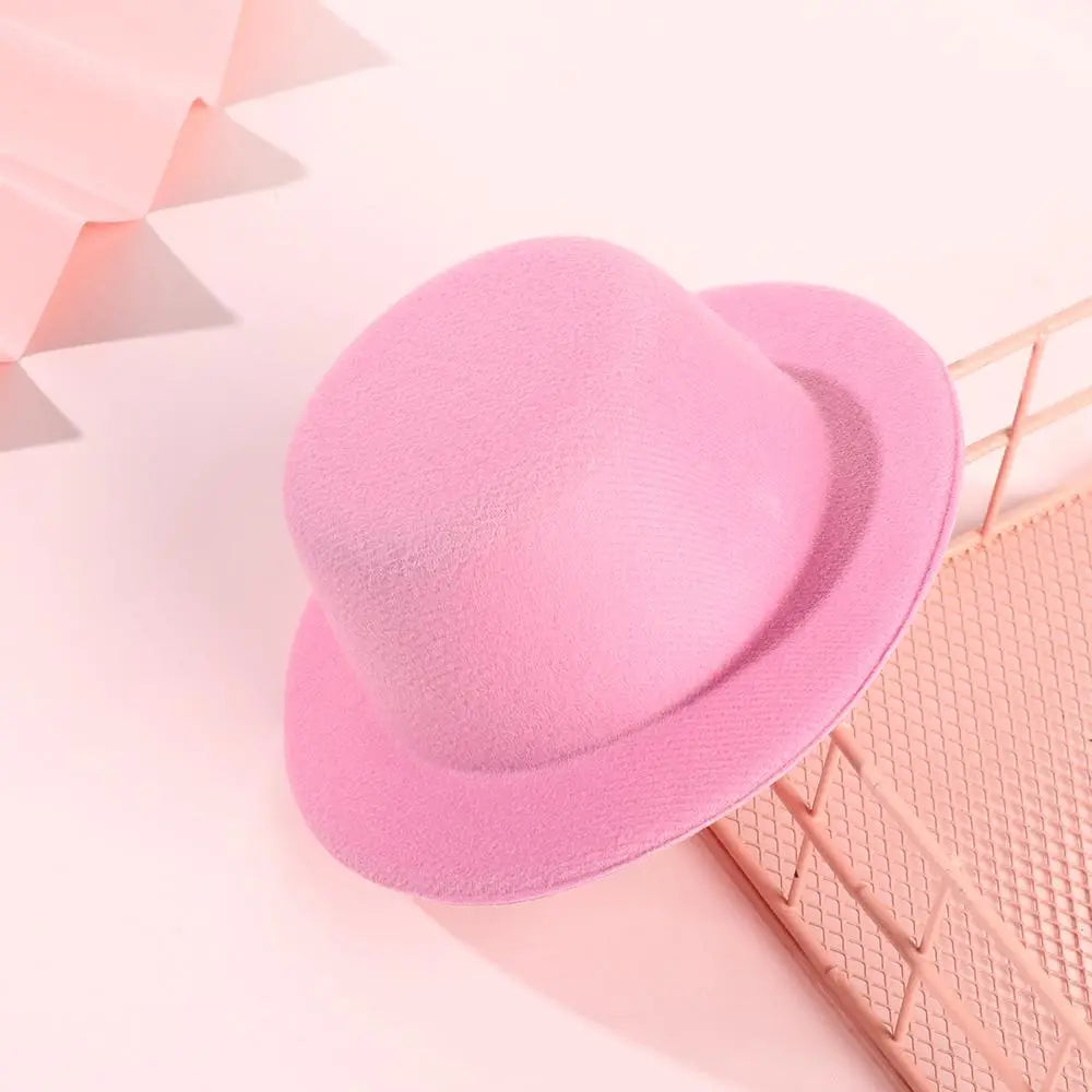 Un chapeau melon (bowler) en feutre rose tendre, à calotte arrondie et bord légèrement incurvé, conçu comme accessoire de mode pour chapeau de poupée en peluche pour des poupées de 60 cm.