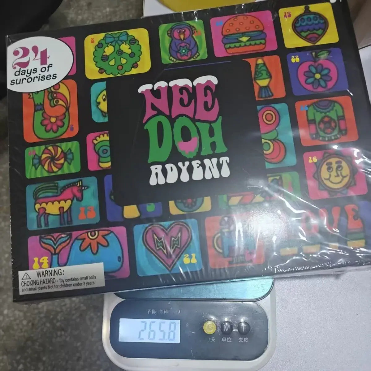 Un calendario de adviento de Halloween Nee Doh colorido con comida de caricatura vibrante y personajes fantásticos en rosa intenso, verde, amarillo y azul sobre un fondo negro, que presenta juguetes blandos espeluznantes.