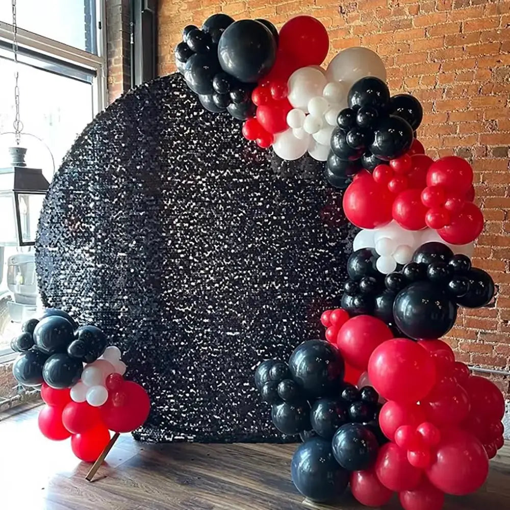 Schwarzes und goldenes Ballonbogen-Set für Partys mit einer schwarzen, mit Pailletten besetzten runden Rückwand, verziert mit Clustern aus roten, schwarzen und weißen Ballons.