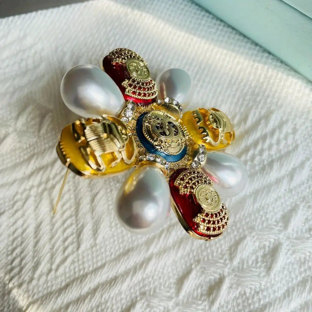 Épingle sertie de rhinestones en forme de coléoptère pour broche de perles designer, au ton doré, avec des accents d’émail rouge et bleu, des pierres à l’aspect de perles et une composition métallique détaillée.