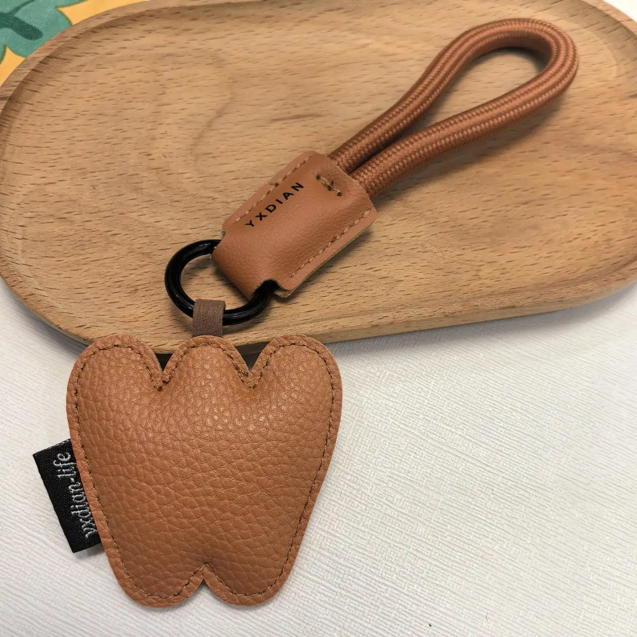Tan leather tooth-shaped keychain featuring a braided cord and black metal ring for use as a leather initial keychain letter wristband charm.