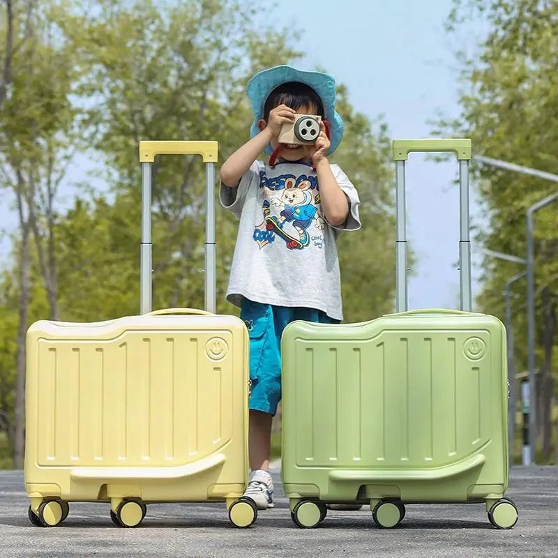 Un enfant portant un chapeau bleu et tenant un appareil photo se tient entre deux valises de voyage pour enfants à coque rigide, de couleur pastel, de couleur jaune, avec des poignées et des roues jaunes.