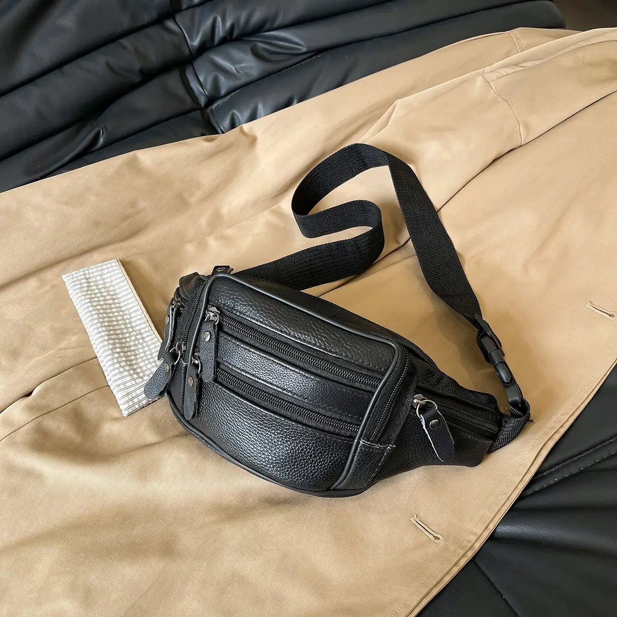 Schwarze Gürteltasche aus echtem Leder mit gepunkteter Struktur, mehreren Reißverschlüssen und einem verstellbaren Riemen zur Verwendung als Crossbody- oder Bauchtasche.