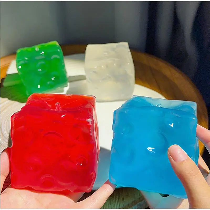 Lebendige transluzente Würfel aus rotem, blauem, grünem und klarem, farbenfrohem Vaseline-Käse-Quetschspielzeug mit strukturierter Oberfläche, von vorn betrachtet.