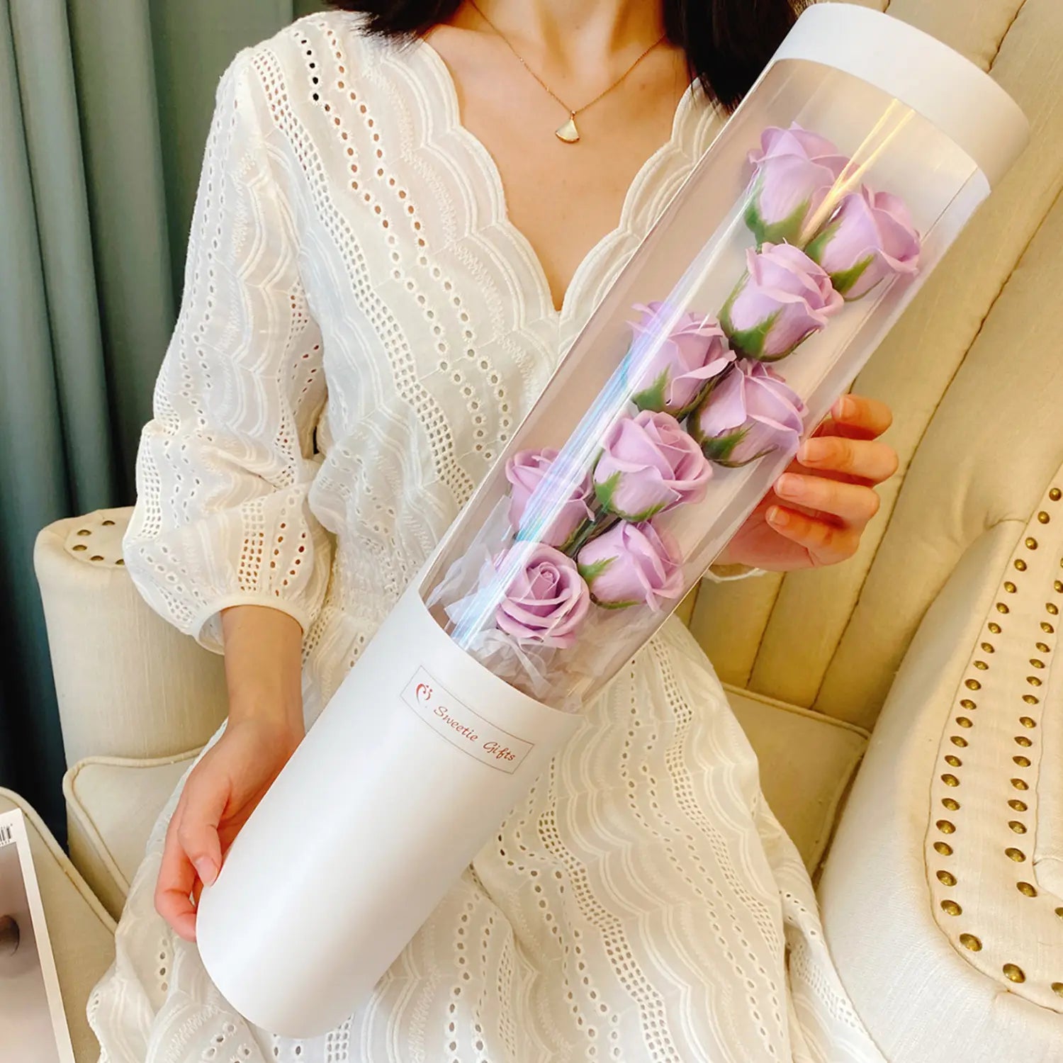 Ein zylindrischer, klarer Schlauch mit weißem Sockel, der konservierte Lavendelrosen für eine LED-Rosen-Seifenblumen-Geschenkschachtel für den Valentinstag enthält