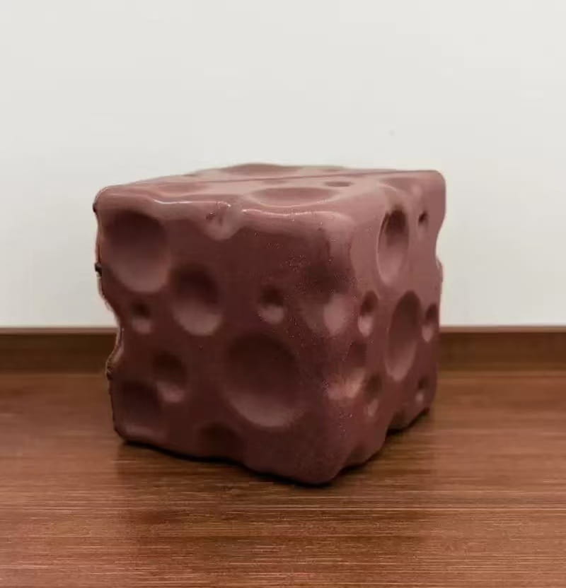 Ein mattes roségoldenes Käse-Soft-Glücksbringer-Spielzeug zur Stressreduktion in Würfelform mit einer porösen, blasenartigen Textur.